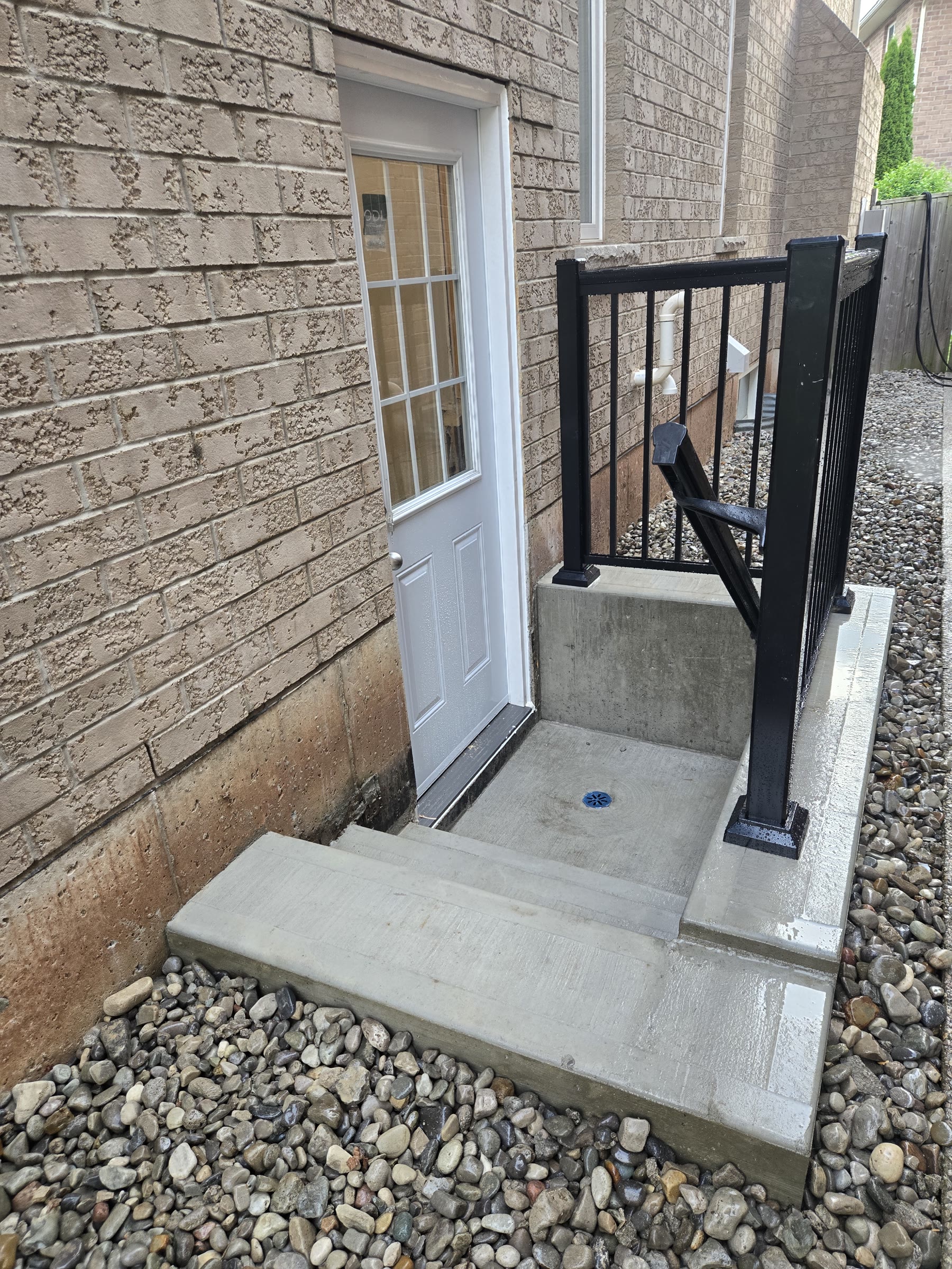 Finished basement side entrance with concrete steps, exterior door and black guardrail